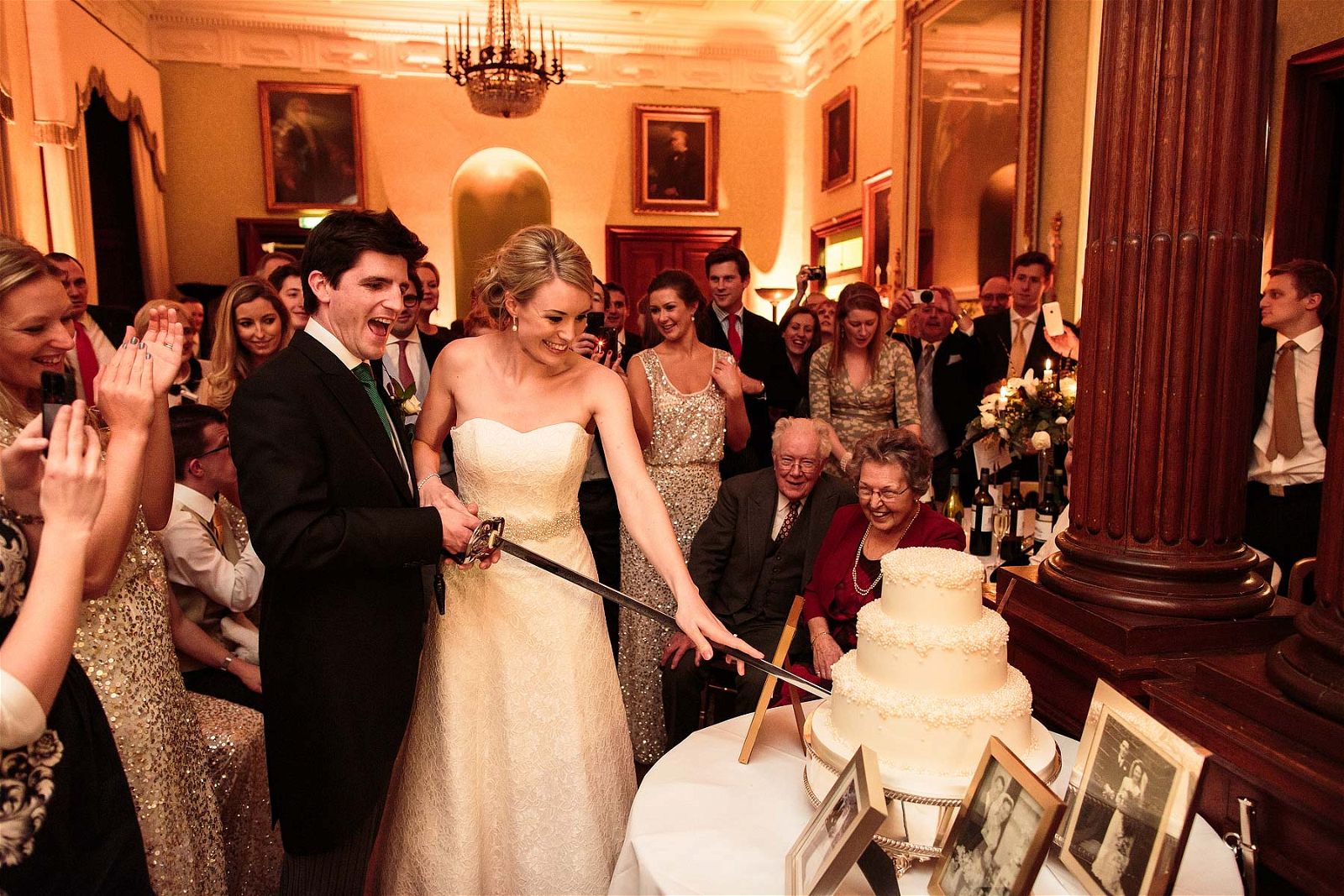 Such a wonderful reaction as the Bride and Groom cut their wedding cake with the grooms sword at Sandon Hall in Stafford by Staffordshire Documentary Wedding Photographer Stuart James